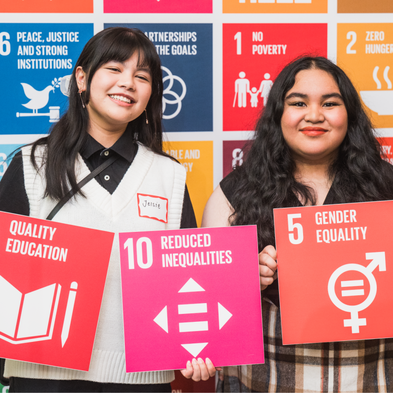 Two student winners holding colourful SDG tiles of Quality Education, Reduced Inequalities and Gender Equality.