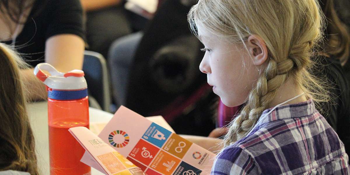 A student looks at a colourful pamphlet with Sustainable Development Goals icons on it.