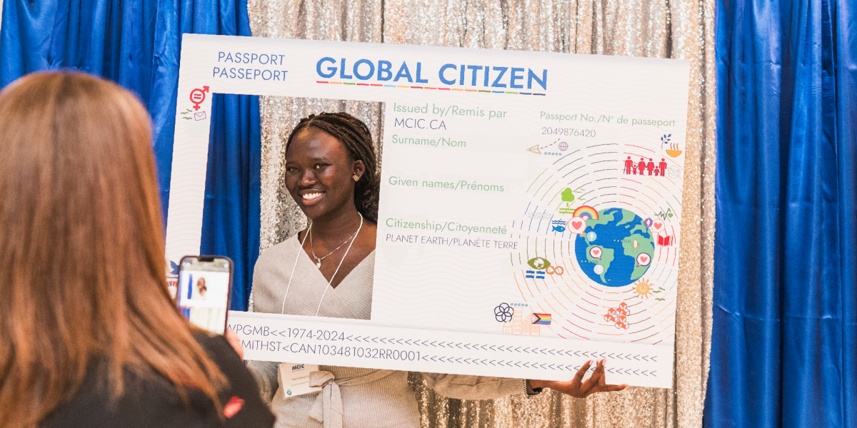 A woman gets their photo taken while holding up a large photo prop of a global citizen passport