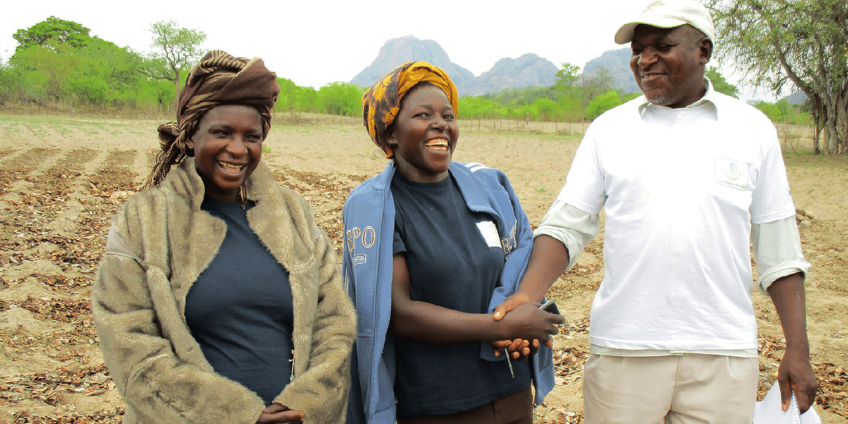 Three people stand together smiling on a farm in Zimbabwe