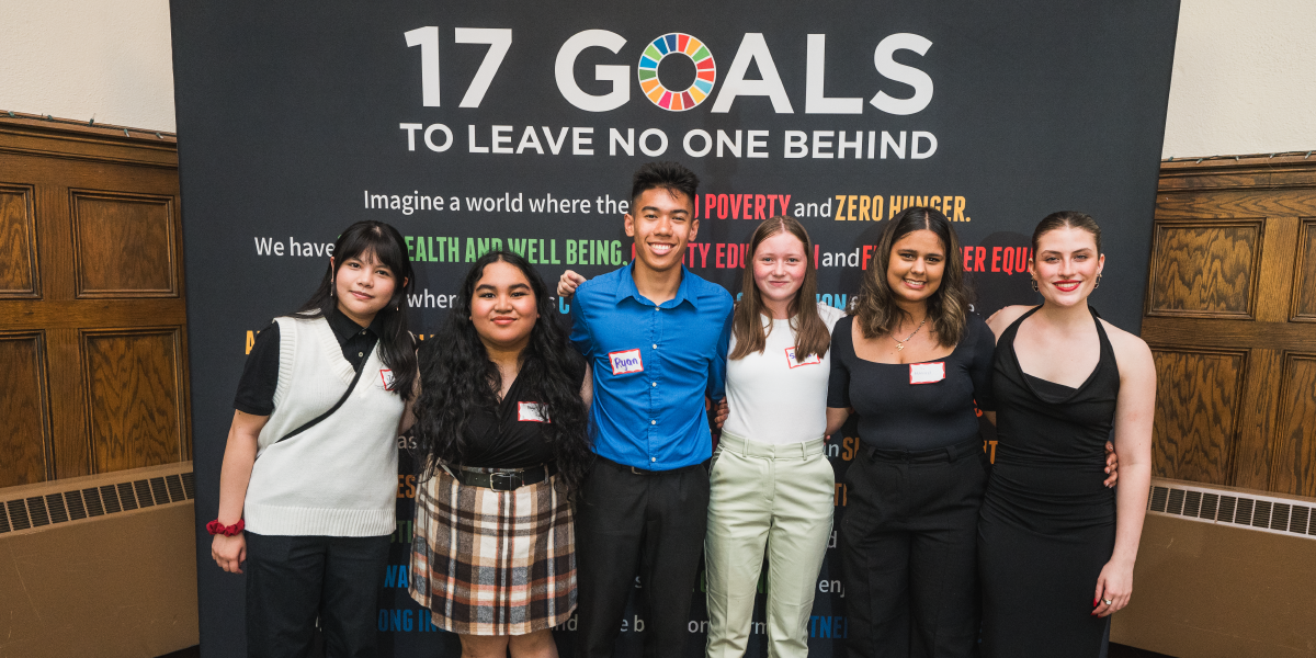 Young award recipients stand together holding certificates, in front of a background with Sustainable Development Goals.