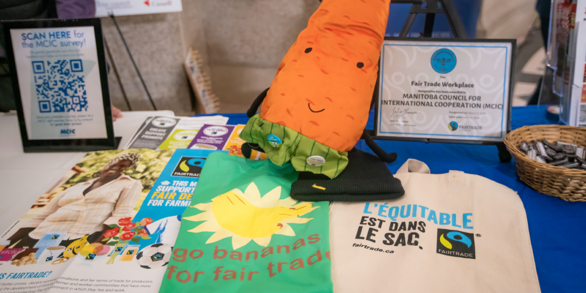 Table showcasing fair trade items including posters, tshirts, bags and a plushy carrot