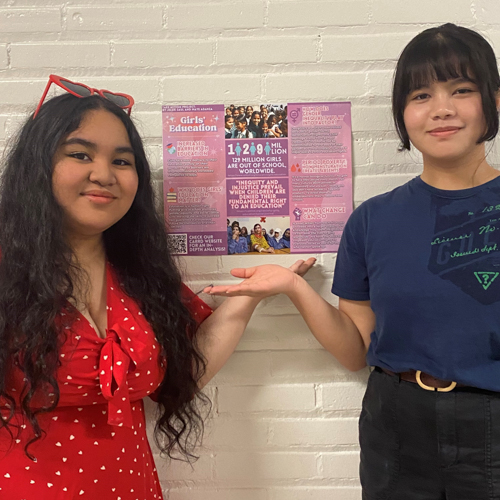 Maye and Jelsie pose next to a poster they created for their Take Action project.